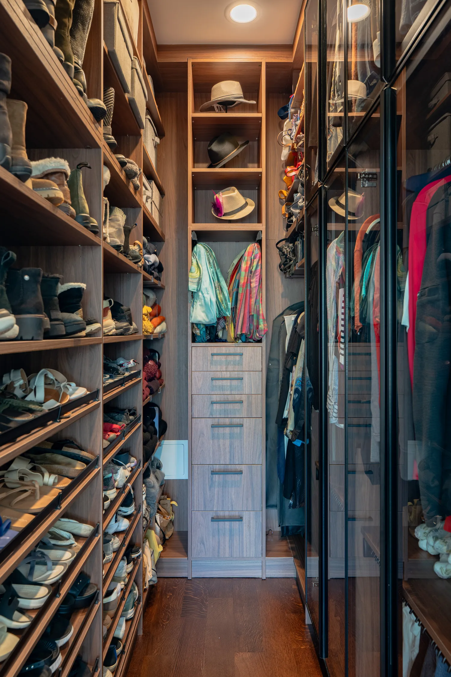 A walk-in closet with walnut shelving and glass wardrobe doors
