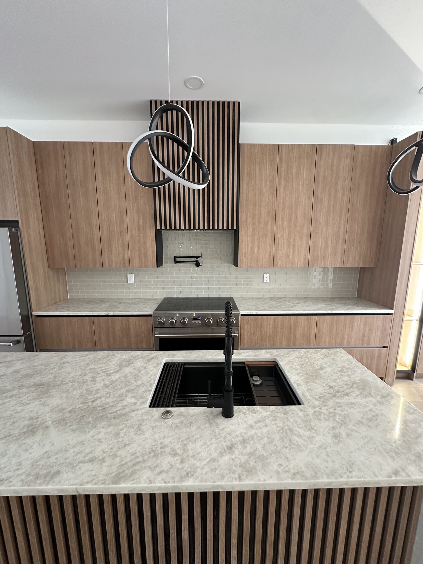 Range wall in oak with a slat panel behind the hood, and a waterfall stone island with an integrated sink.